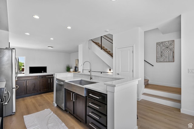 kitchen featuring dark brown cabinetry, appliances with stainless steel finishes, a center island with sink, a sink, and recessed lighting