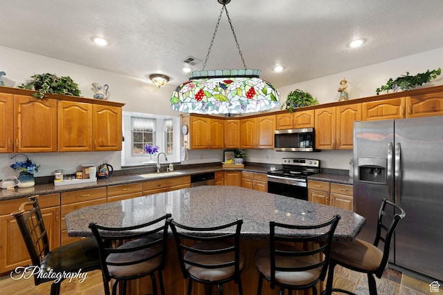 kitchen featuring brown cabinetry, visible vents, a center island, a sink, and stainless steel appliances