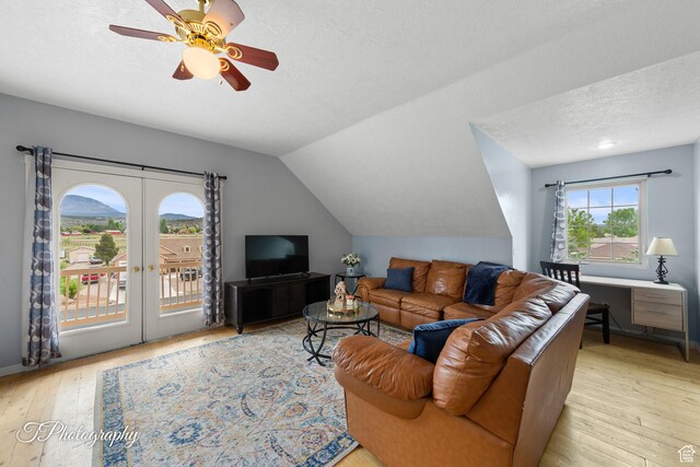 living area with ceiling fan, a textured ceiling, french doors, light wood-type flooring, and vaulted ceiling