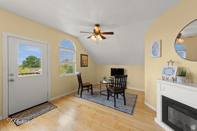 office featuring ceiling fan, a glass covered fireplace, baseboards, wood finished floors, and lofted ceiling