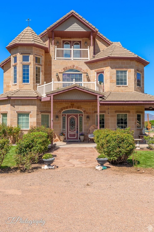 view of front of house featuring a tile roof, a balcony, and stone siding