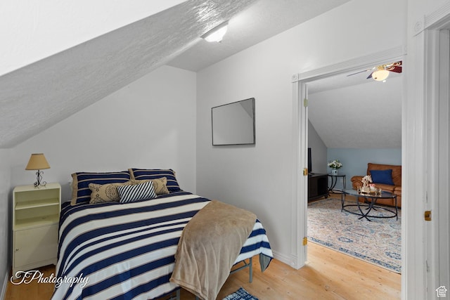 bedroom with wood finished floors, a textured ceiling, baseboards, and lofted ceiling