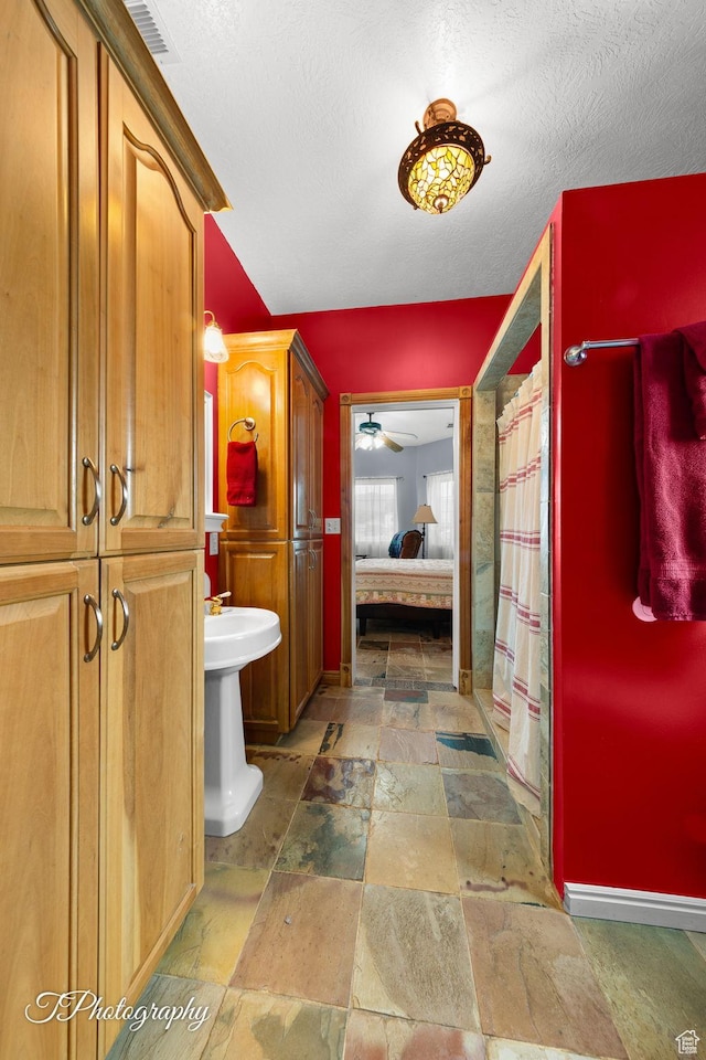 full bathroom featuring ceiling fan, a textured ceiling, stone tile floors, ensuite bath, and a shower with shower curtain