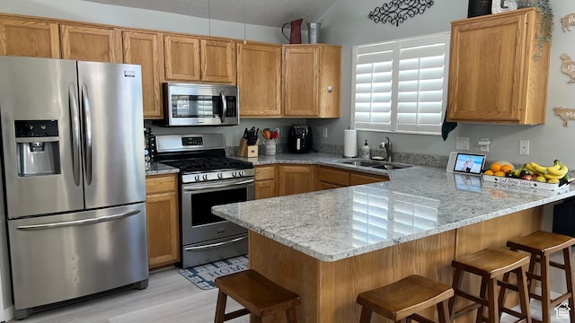 5026 S 1150 E, South Ogden, UT 84403 - kitchen featuring a peninsula, a kitchen bar, a sink, light wood-style flooring, and appliances with stainless steel finishes