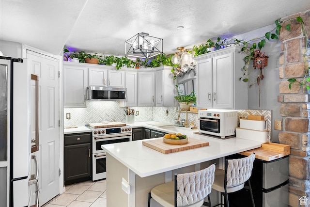 929 W 670 S Unit 8, Pleasant Grove, UT 84062 - kitchen featuring a notable chandelier, a peninsula, stainless steel microwave, decorative backsplash, and double oven range