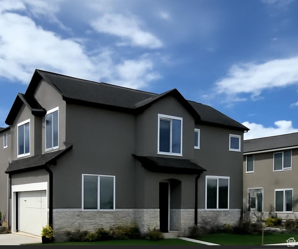 view of front facade with an attached garage, stucco siding, a front yard, and stone siding