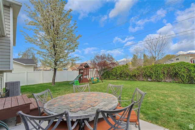 view of patio featuring a fenced backyard, central AC unit, outdoor dining space, and a playground
