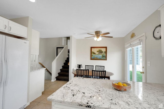 kitchen with a ceiling fan, light stone countertops, light tile patterned floors, freestanding refrigerator, and white cabinetry