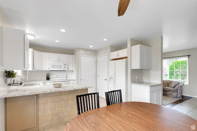 kitchen with a peninsula, white appliances, light tile patterned floors, a sink, and backsplash