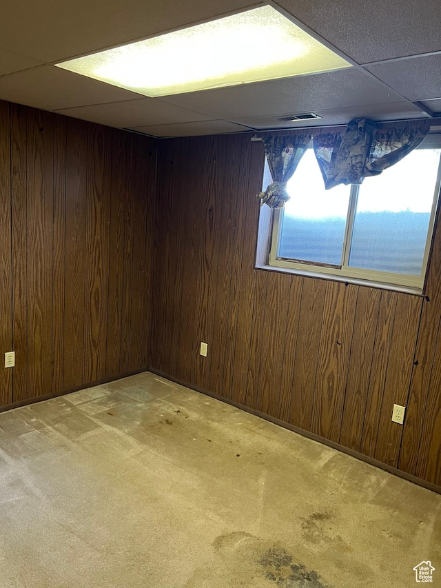 below grade area featuring carpet floors, wood walls, and a drop ceiling