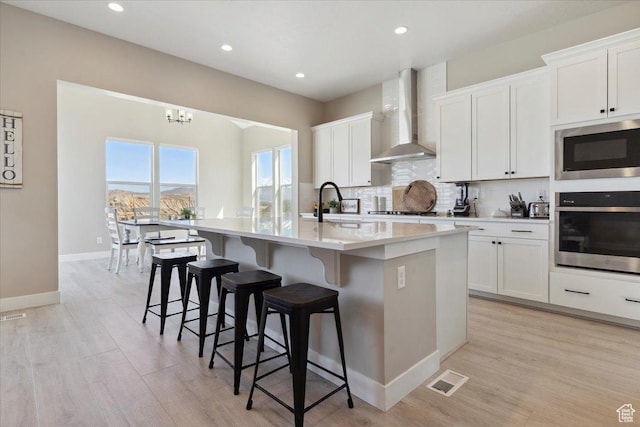 304 E Empire Springs Dr, Saratoga Springs, UT 84045 - kitchen featuring appliances with stainless steel finishes, wall chimney exhaust hood, tasteful backsplash, a breakfast bar, and a kitchen island with sink