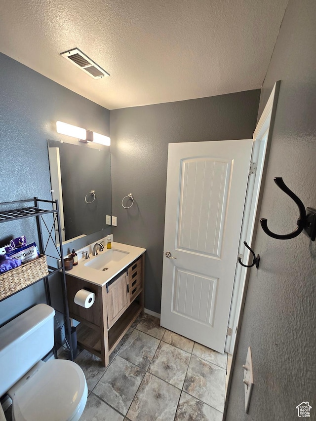 bathroom featuring visible vents, a textured ceiling, and a textured wall