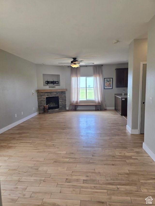 unfurnished living room with light wood-style floors, baseboards, a ceiling fan, and a fireplace