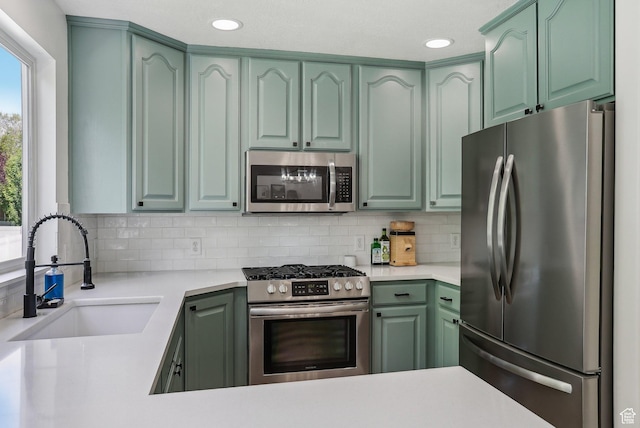 kitchen featuring appliances with stainless steel finishes, a sink, green cabinets, backsplash, and light countertops