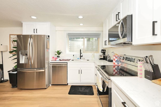 kitchen with white cabinets, appliances with stainless steel finishes, a sink, light wood-style floors, and a textured ceiling