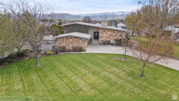 mid-century modern home with a mountain view, a front yard, and stone siding