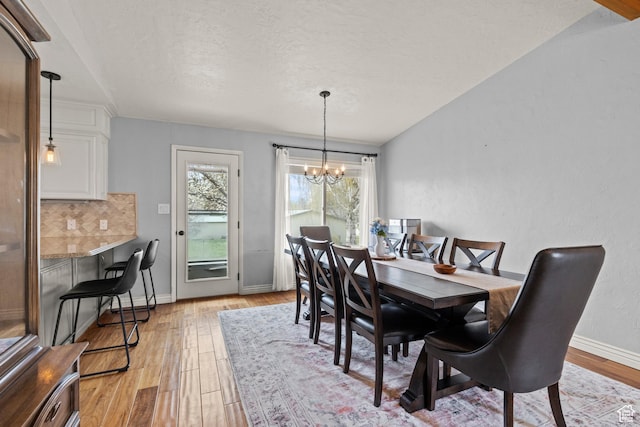 dining space with a textured ceiling, baseboards, a chandelier, and light wood finished floors