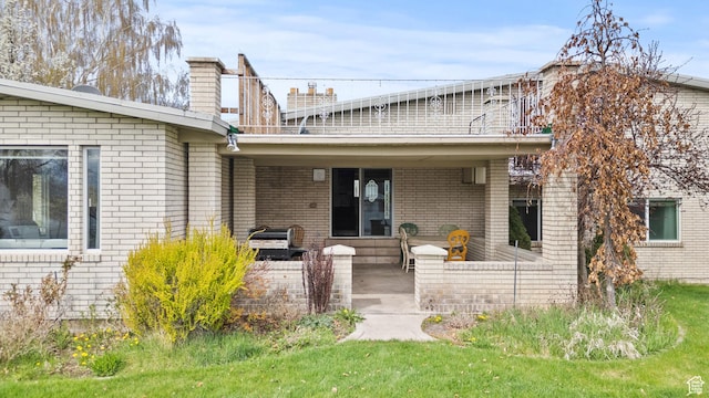 back of property with a yard, brick siding, a chimney, and a patio area