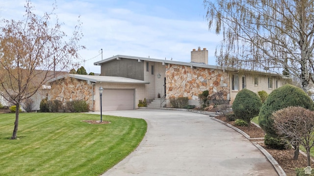 mid-century modern home featuring aphalt driveway, a garage, stone siding, a front yard, and a chimney