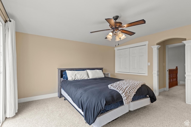 bedroom with light colored carpet, arched walkways, decorative columns, and baseboards