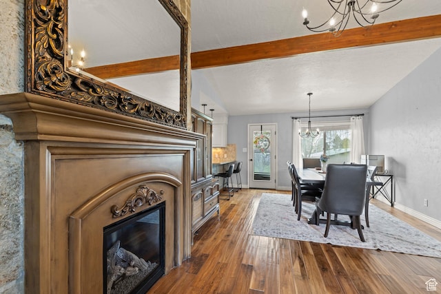 dining space featuring dark wood-style flooring, a chandelier, lofted ceiling with beams, and a glass covered fireplace