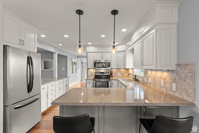 kitchen featuring a peninsula, light wood-type flooring, white cabinets, a sink, and stainless steel appliances