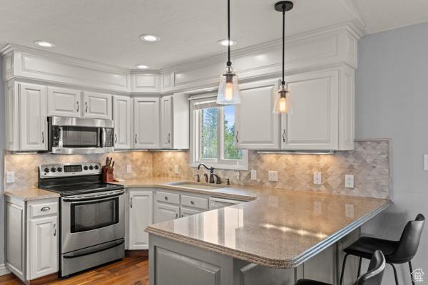 kitchen featuring a sink, stainless steel appliances, a peninsula, and white cabinetry