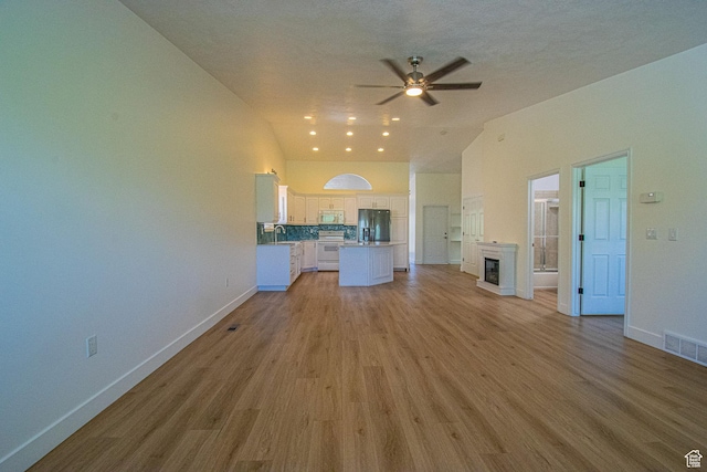 25 Clubhouse Dr, Stansbury Park, UT 84074 - unfurnished living room featuring ceiling fan, visible vents, light wood-style floors, baseboards, and vaulted ceiling