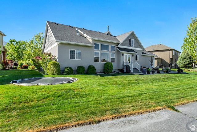rear view of property featuring a lawn, a trampoline, stucco siding, and roof with shingles
