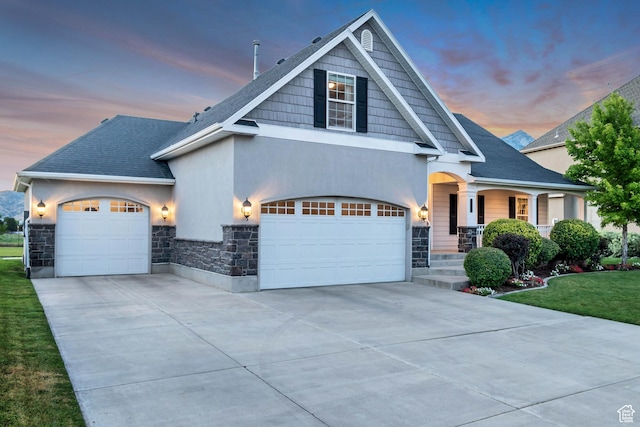 view of front of home featuring a front lawn, covered porch, stone siding, stucco siding, and concrete driveway