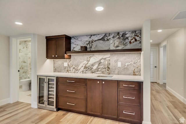 bar with a sink, beverage cooler, indoor wet bar, decorative backsplash, and light wood-type flooring