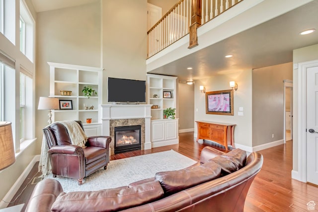 living area with a tiled fireplace, baseboards, wood finished floors, and a towering ceiling