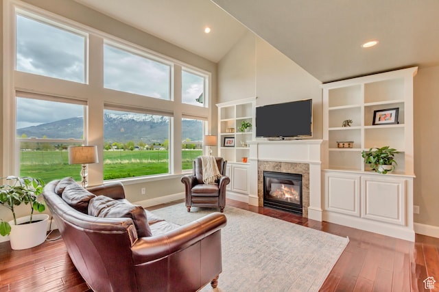 living room featuring hardwood / wood-style floors, high vaulted ceiling, baseboards, and a tile fireplace