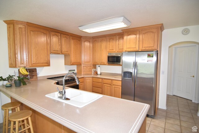 183 E Ama Fille Ln N, Elk Ridge, UT 84651 - kitchen featuring appliances with stainless steel finishes, a peninsula, a sink, light tile patterned floors, and a breakfast bar area