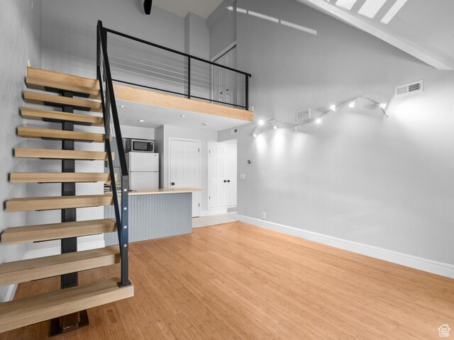 stairs with baseboards, visible vents, high vaulted ceiling, and wood finished floors