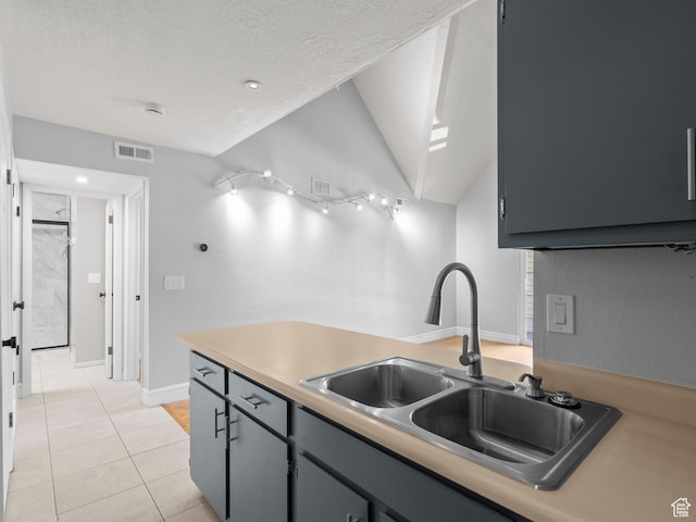 kitchen with light tile patterned floors, a sink, a textured ceiling, visible vents, and lofted ceiling