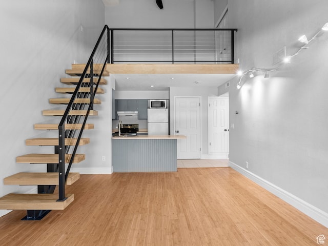 unfurnished living room with baseboards, visible vents, a towering ceiling, stairway, and light wood-type flooring