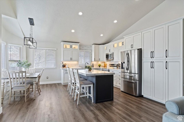 kitchen with a kitchen island, glass insert cabinets, stainless steel appliances, light countertops, and vaulted ceiling