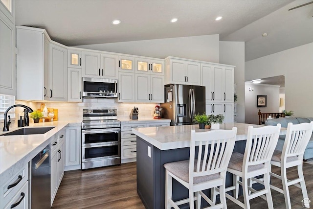 kitchen featuring a sink, vaulted ceiling, backsplash, white cabinets, and appliances with stainless steel finishes