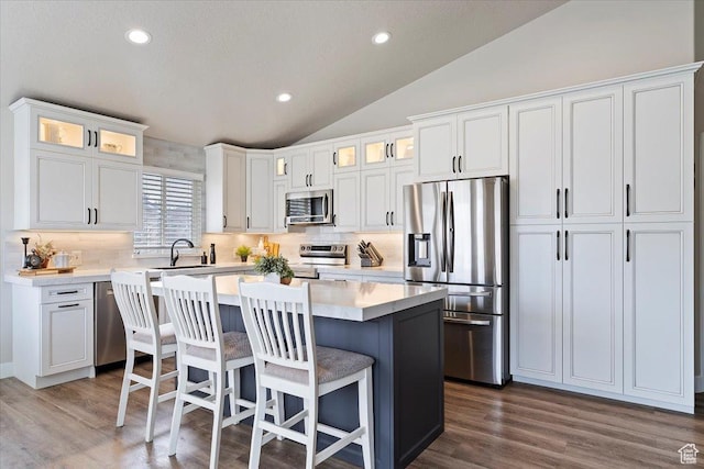kitchen with lofted ceiling, a sink, decorative backsplash, a kitchen island, and stainless steel appliances