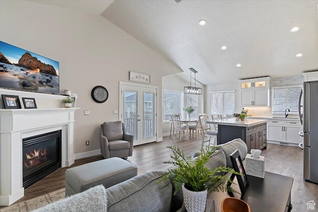 living room featuring a textured ceiling, baseboards, a glass covered fireplace, high vaulted ceiling, and wood finished floors