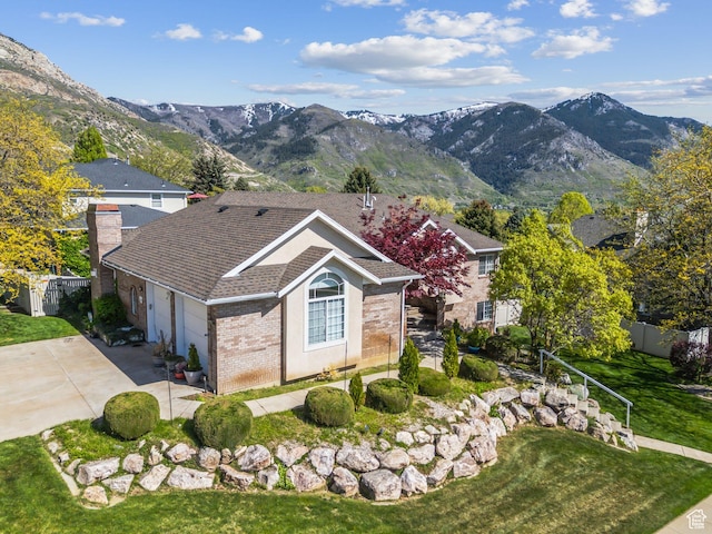 view of front of home featuring fence, a mountain view, brick siding, concrete driveway, and a chimney