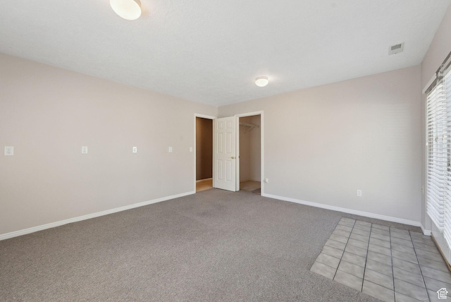 unfurnished bedroom with light colored carpet, a walk in closet, baseboards, and visible vents