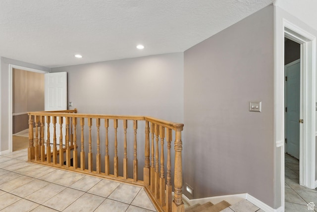 hall featuring light tile patterned floors, an upstairs landing, a textured ceiling, baseboards, and recessed lighting
