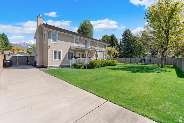 back of property featuring a gate, stucco siding, a fenced backyard, a lawn, and a playground