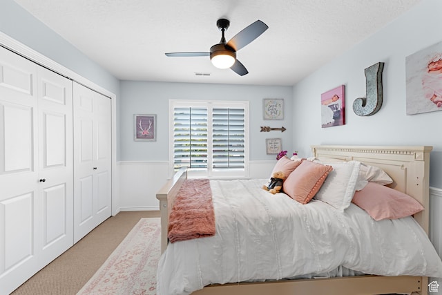 bedroom featuring carpet flooring, a closet, visible vents, wainscoting, and ceiling fan