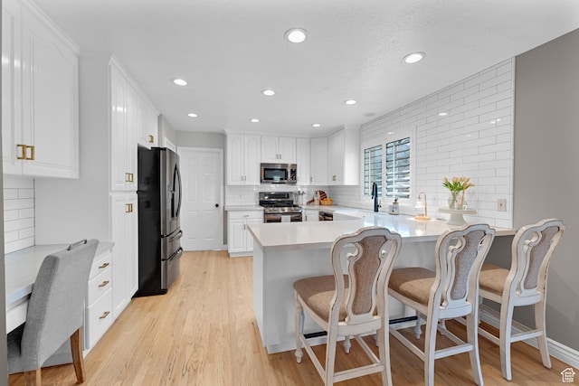 kitchen featuring recessed lighting, a peninsula, backsplash, stainless steel appliances, and white cabinets