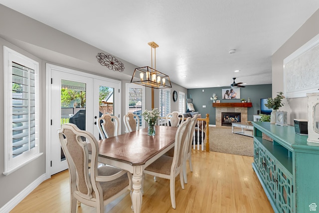 dining area featuring a tile fireplace, plenty of natural light, baseboards, and light wood-style floors