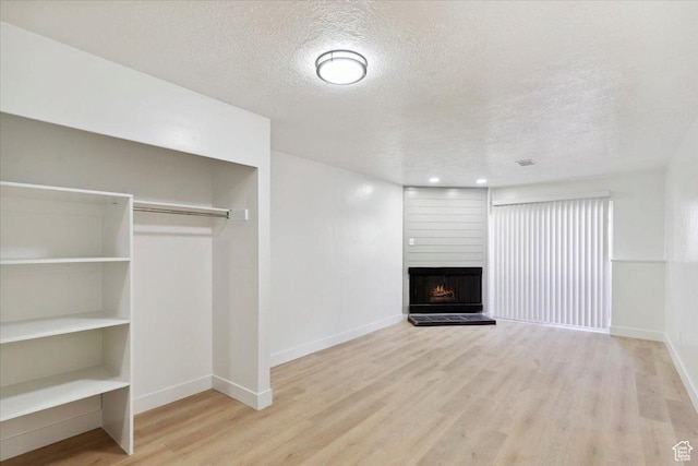 unfurnished living room with a textured ceiling, baseboards, a fireplace, and wood finished floors