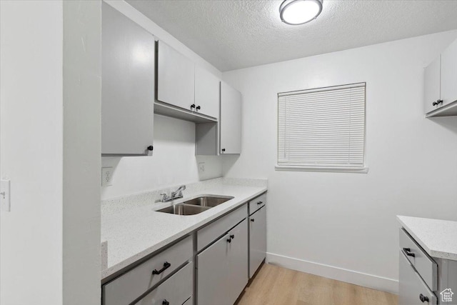 kitchen with a sink, light wood-style flooring, a textured ceiling, and baseboards
